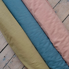 3 Fabric rolls in beige, blue and pastel pink on a wooden background in Stag & Bow haberdashery London